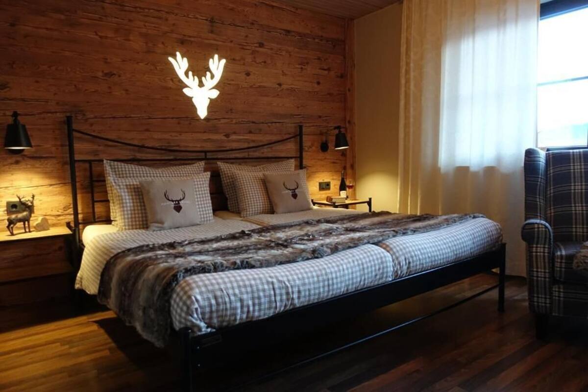 Een slaapkamer met houten lambrisering, een bed, twee nachtkastjes, een stoel en een decoratie van een hertenkop aan de muur.
