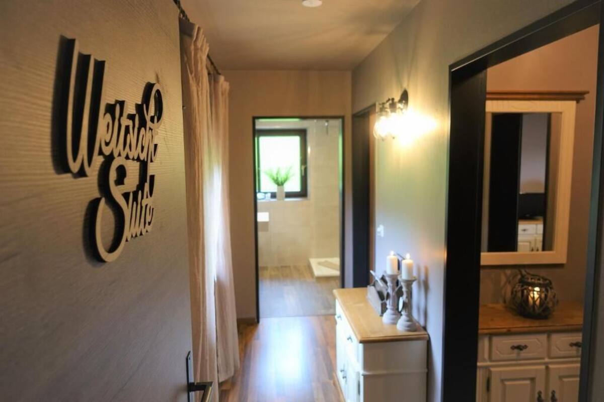 Een gang met een 'Welcome'-bord, een spiegel, een dressoir en een raam met een plant.