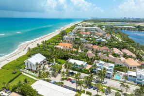 An aerial view of a coastal residential area with houses, a beach, and a golf course.