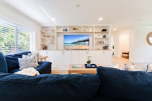 A modern living room with a large flat-screen TV, a blue sofa, and a wooden coffee table. - The Sandstone at Juno Beach | 11 | Rooftop Deck! (Juno Beach)
