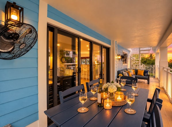 An outdoor dining area with a table set for two, a fan, and a view of the interior.