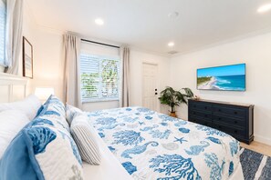 A bedroom with a bed, a dresser, a plant, a window with blinds, and a painting on the wall. - Designer Beachside Serenity– Steps to the Beach! (Juno Beach)