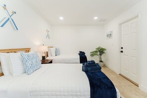 Una habitación de hotel con dos camas, una mesita de noche, una lámpara, una planta y una puerta.