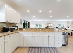 A modern kitchen with white cabinetry, granite countertops, a built-in microwave, and a stainless steel dishwasher. - Designer Beachside Serenity– Steps to the Beach! (Juno Beach)