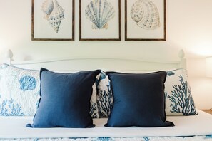 A bed with a white headboard, two dark blue pillows, and a white bedspread with blue sea-themed designs.