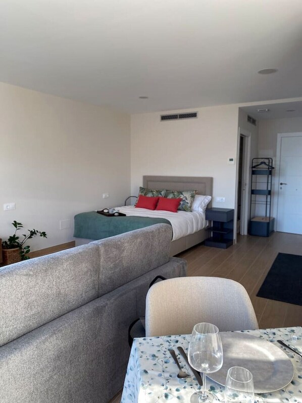 A compact hotel room with a single bed, a small table with a tablecloth, and a sofa. - Apartamento Alborada 1 (Moaña)