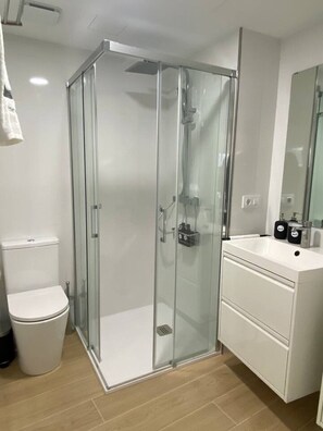 A modern bathroom with a glass-enclosed shower, a white toilet, and a sink with a mirror above it. - Apartamento Alborada 1 (Moaña)