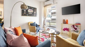 Een moderne woonkamer met een bank, fauteuils, een salontafel en een aan de muur bevestigde televisie.