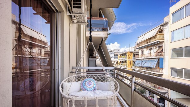 Een balkon met een witte rieten stoel, een tafeltje en een decoratief kussen.