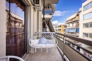 A balcony with a white wicker chair, a small table, and a patterned cushion. - Stylish Family Flat   – Balcony & Metro Access (Dafni)