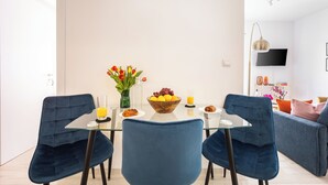 Een moderne eetruimte met een glazen tafel, blauwe stoelen, een fruitschaal en een bloevas.
