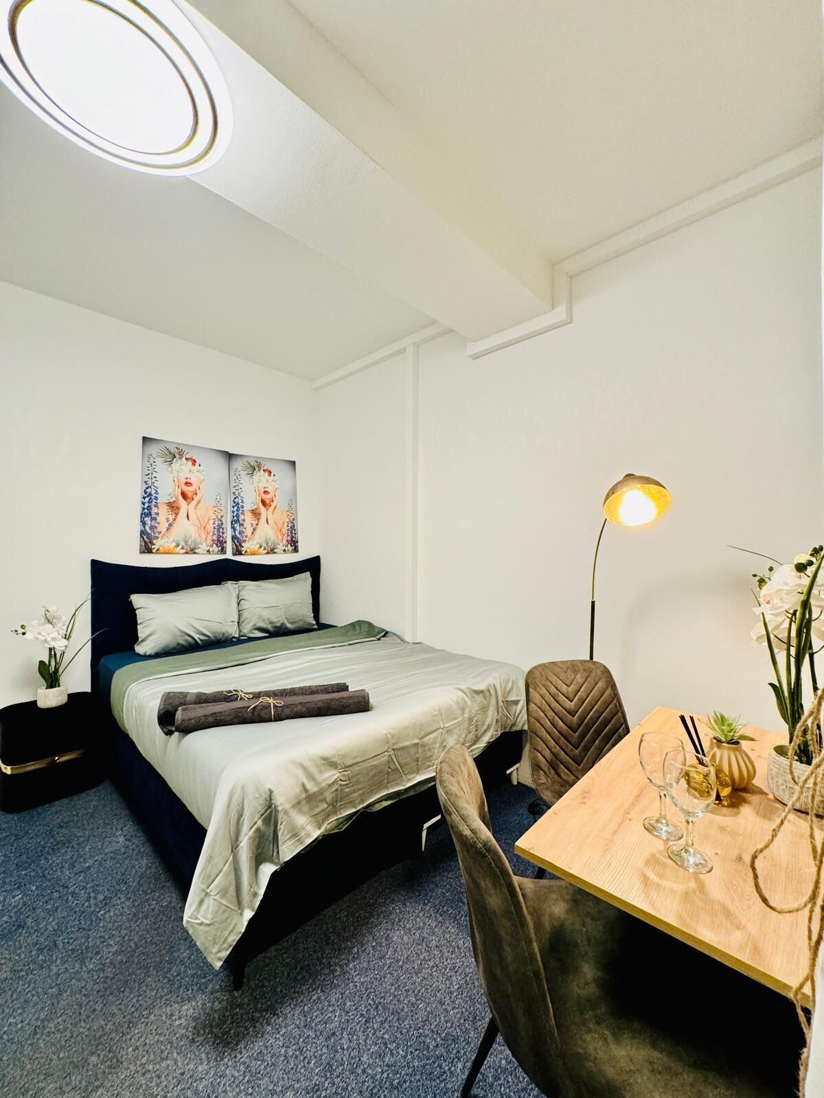 A modern bedroom with a bed, bedside table, lamp, and a small dining table with a chair.