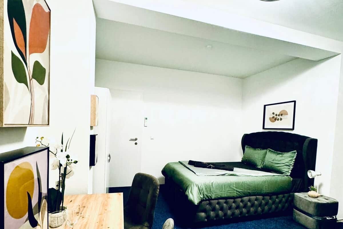 A compact bedroom with a bed, a desk, and chairs. There are framed pictures on the wall.
