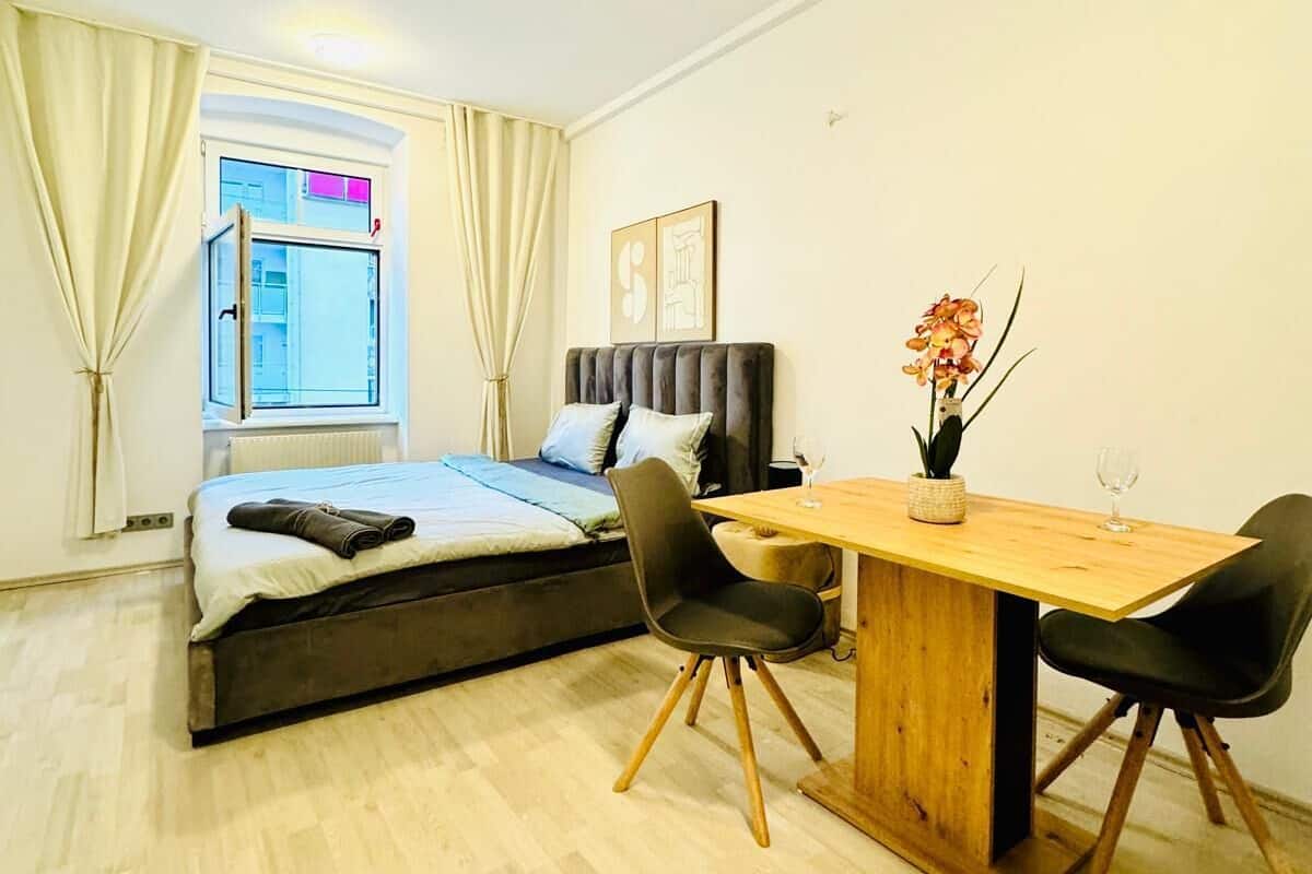 A modern bedroom with a bed, bedside table, and a small dining area with chairs and a table.