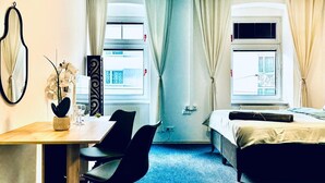 A compact hotel room with a desk, two chairs, a bed, and two windows with curtains. - Spacious 7BR Apartment Prime Location (Vienna)