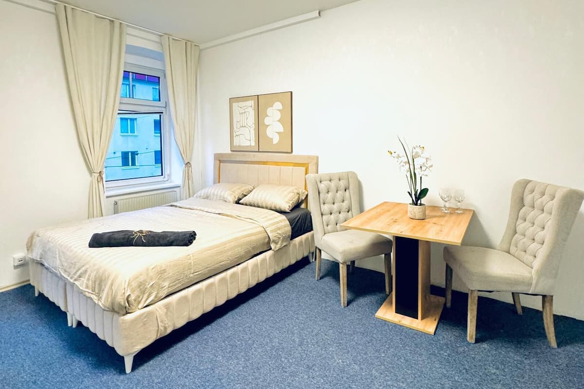 A hotel room with a bed, a small table with two chairs, and a window with curtains.