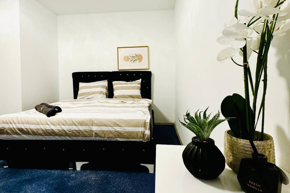 A bedroom with a bed, a framed picture on the wall, and a potted plant on a bedside table.