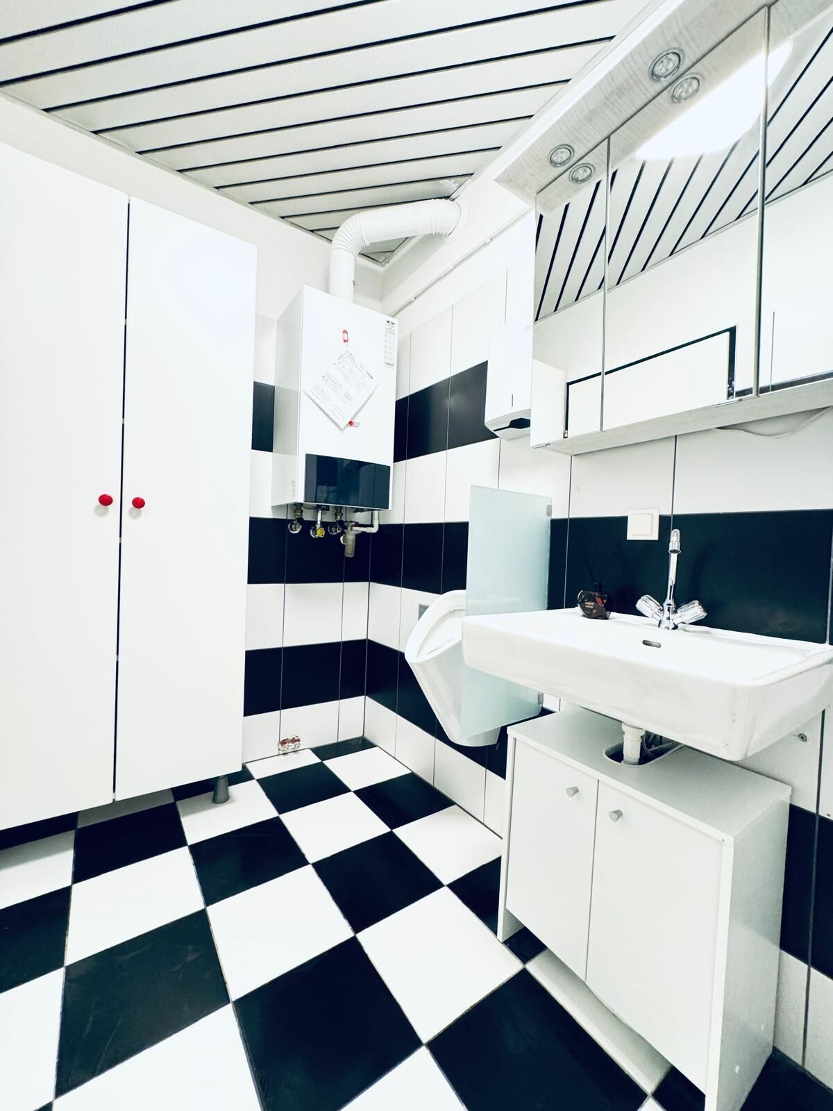 Ein modernes Badezimmer mit einem schwarz-weißen Schachbrettfußboden, weißen Schränken und einem weißen Waschbecken.