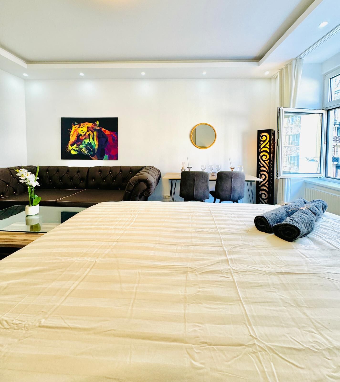 Una habitación de hotel con cama, sofá, mesa de comedor con sillas, espejo y ventana.