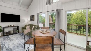 A room with a round wooden table, a sofa, a TV mounted on the wall, and a balcony with a view of greenery. - D4 Creekside Walk to Convention and The Landing (Branson)