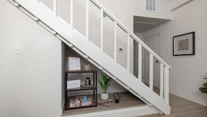 A staircase with white railings, a black metal shelf with books and a framed certificate, and a potted plant on the landing. - D4 Creekside Walk to Convention and The Landing (Branson)