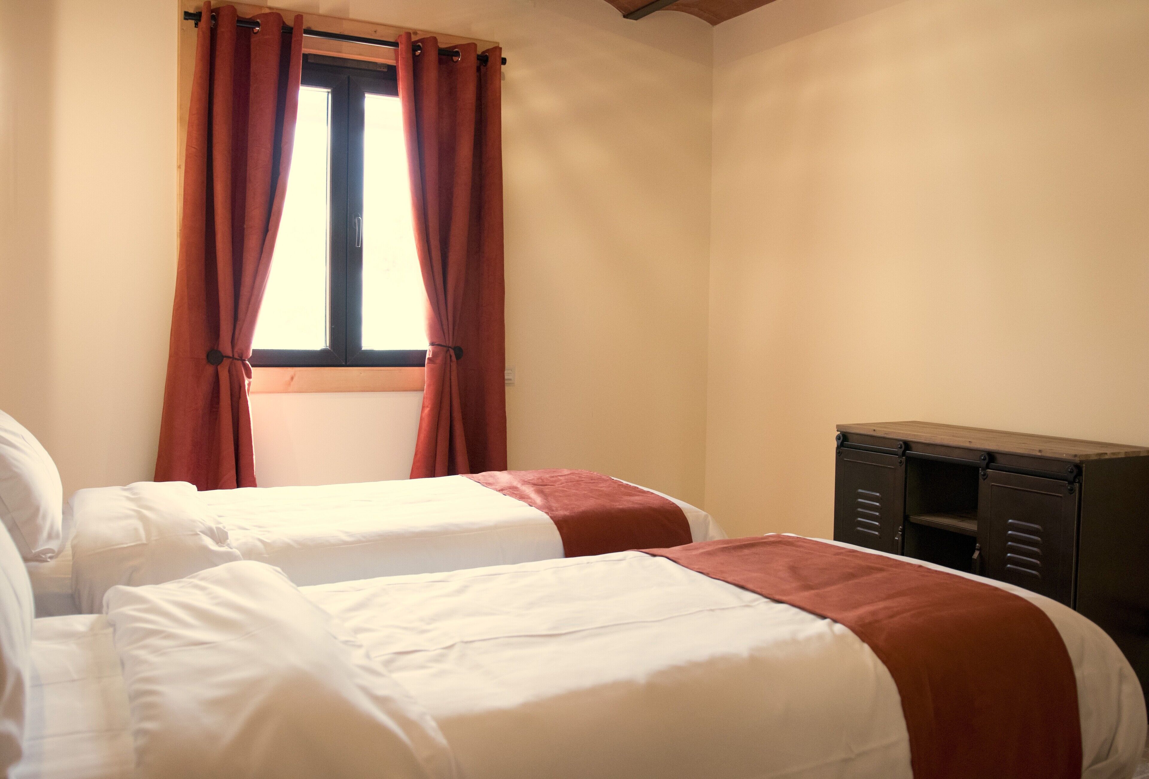 A room with two beds, a window with curtains, and a wooden cabinet.