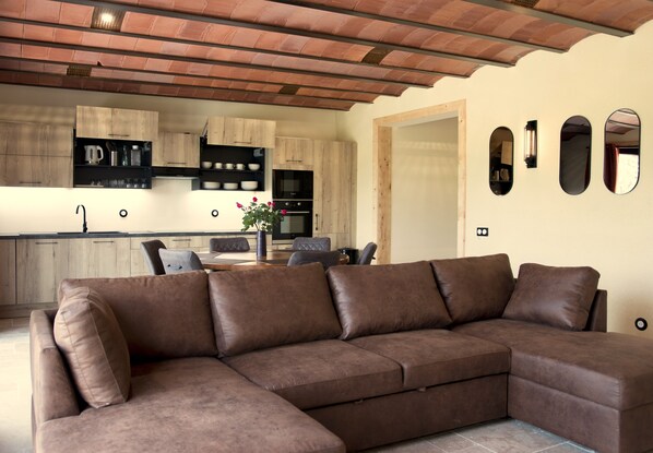 Une cuisine moderne avec des meubles en bois, un coin repas comprenant une table et des chaises, et un canapé d’angle en cuir marron.