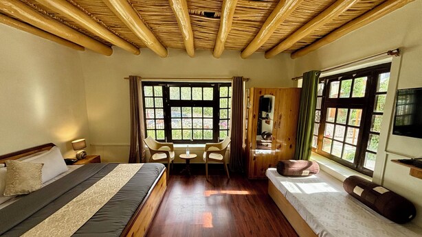A bedroom with a bed, a desk, a chair, a wardrobe, and large windows. - City Heart Boutique Stays (Leh)