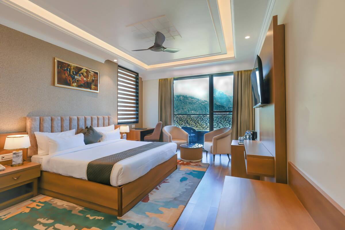 Habitación de hotel con una cama grande, un escritorio, una silla, un televisor y una ventana con vista a la montaña.