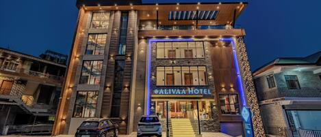 Un hotel moderno con un letrero llamativo, una escalera que conduce a la entrada y dos coches estacionados en la parte delantera.