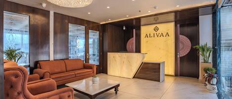 A modern lobby with a reception desk, a large chandelier, and a seating area with a sofa and coffee table.