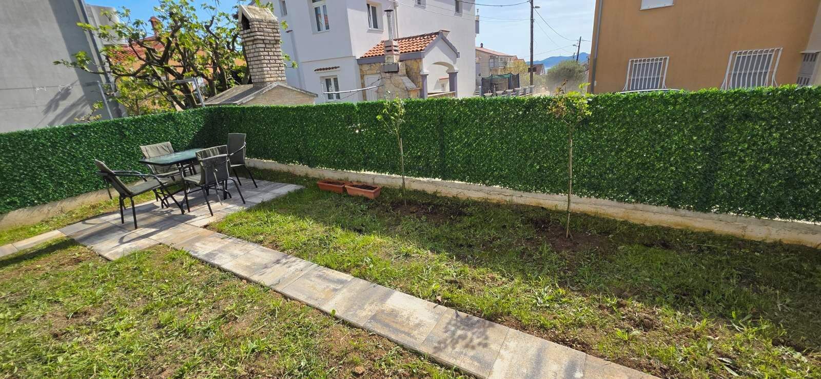 A patio area with a table and chairs, a neatly trimmed hedge, and a pathway.