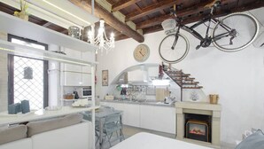 A modern kitchen with white cabinets, a dining area with a sofa and chairs, a fireplace, and a bicycle hanging from the ceiling. - Your nest in Trastevere, the heart of Rome - Your Nest in the Heart of Rome (Roma)