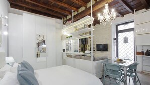A modern bedroom with a bed, a desk, and a TV. There is a chandelier, a window, and a kitchenette. - Your nest in Trastevere, the heart of Rome - Your Nest in the Heart of Rome (Roma)