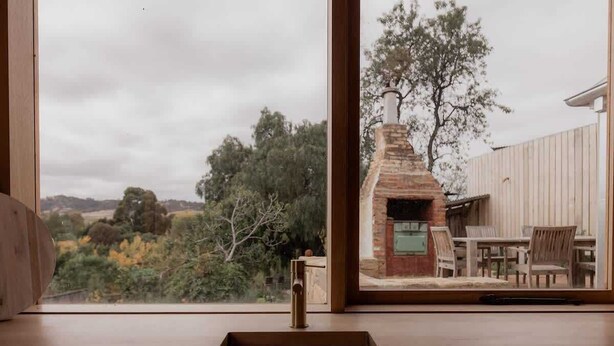 A modern kitchen with a large window overlooking a garden and a brick fireplace. - 'Engineers Hut 1823' in Historic Richmond (Richmond)