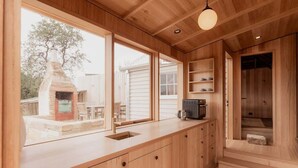 A modern kitchen with wooden cabinetry, a built-in oven, and a large window overlooking a backyard. - 'Engineers Hut 1823' in Historic Richmond (Richmond)