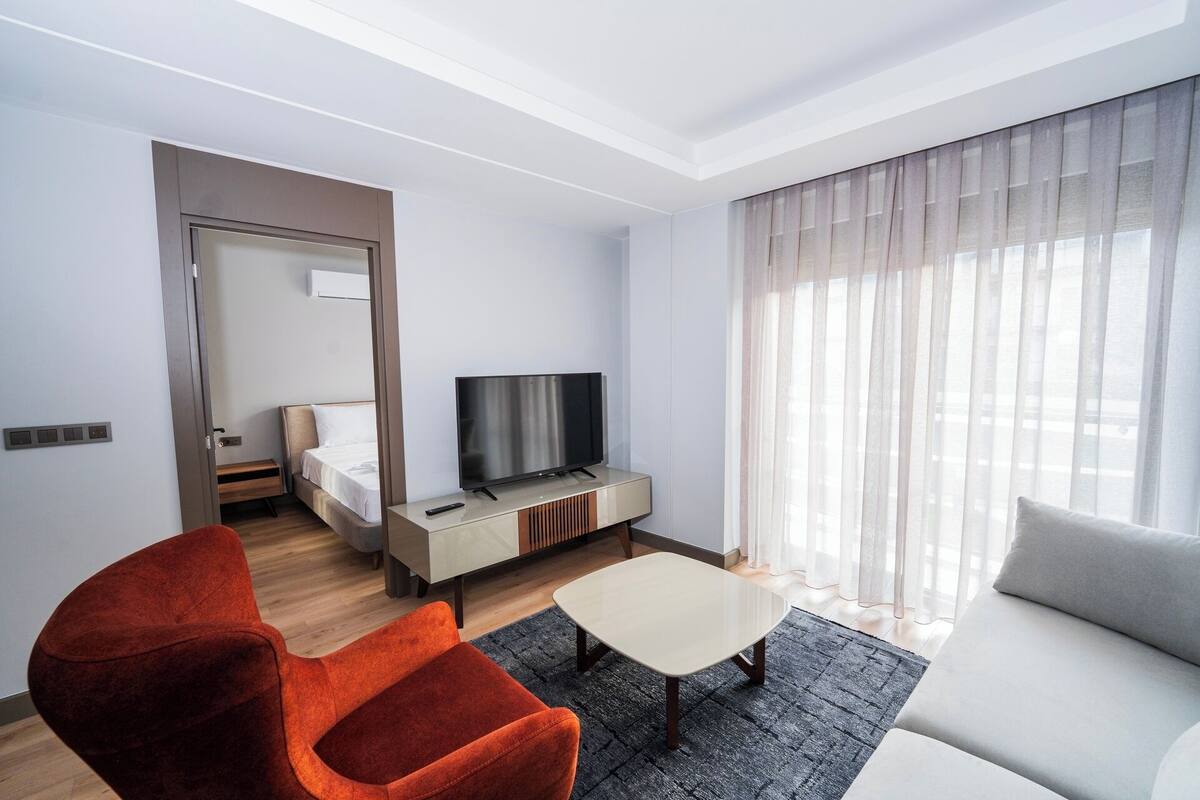 Una habitación de hotel moderna con cama, televisor, sofá y una silla roja.