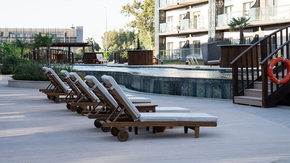 Une rangée de chaises longues à roulettes, une piscine et une bouée de sauvetage sur une terrasse.