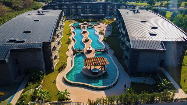 Een hotel met een centraal gelegen zwembad, meerdere balkons en een aangelegde tuin.
