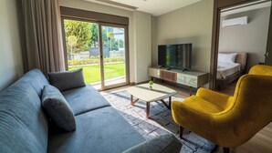 Een moderne hotelkamer met een grijze bank, een gele fauteuil en een televisie op een houten kast.