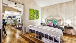 Een moderne slaapkamer met een metalen bedframe, een groene bloemenprint aan de wand, een nachtkastje met een lamp en uitzicht op het aangrenzende keukenvertrek.