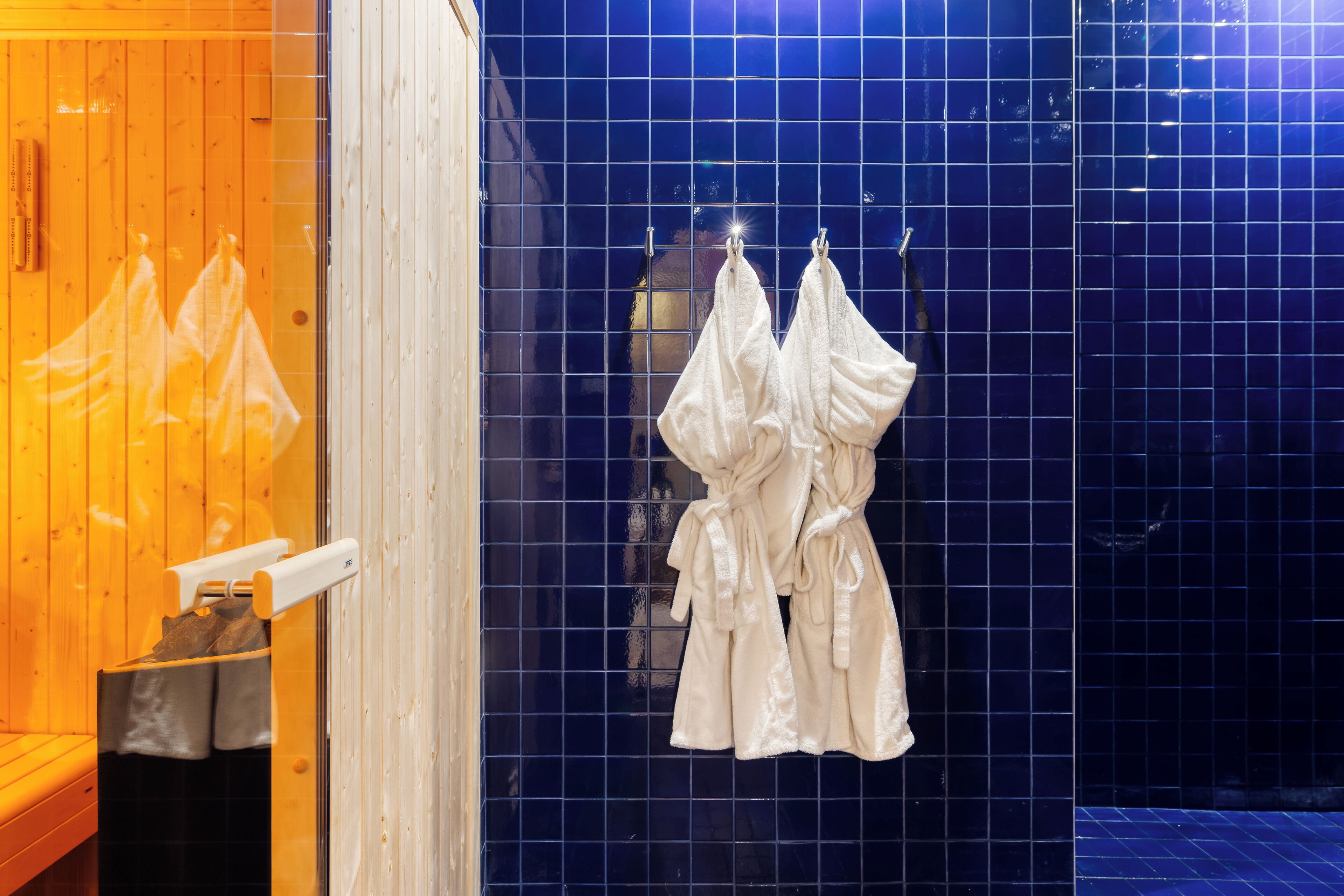 A bathroom with a wooden bench, a towel rack with towels, and a blue tiled wall.