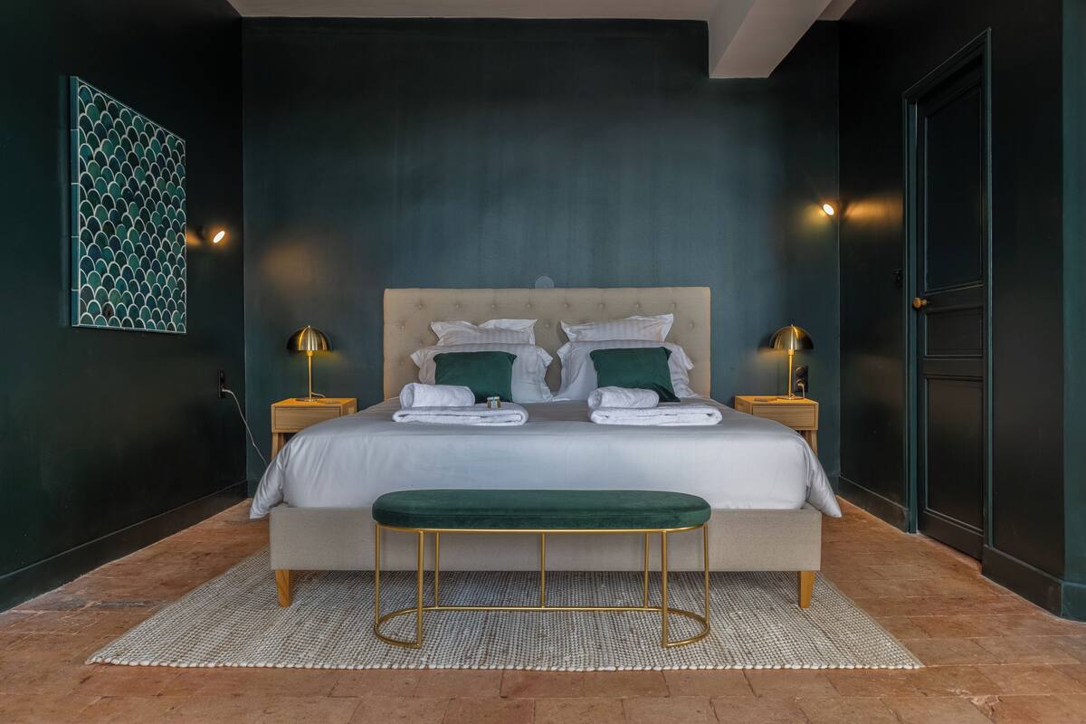 Une chambre à coucher comprenant un lit, deux tables de chevet, un banc, une œuvre d’art murale et une porte.