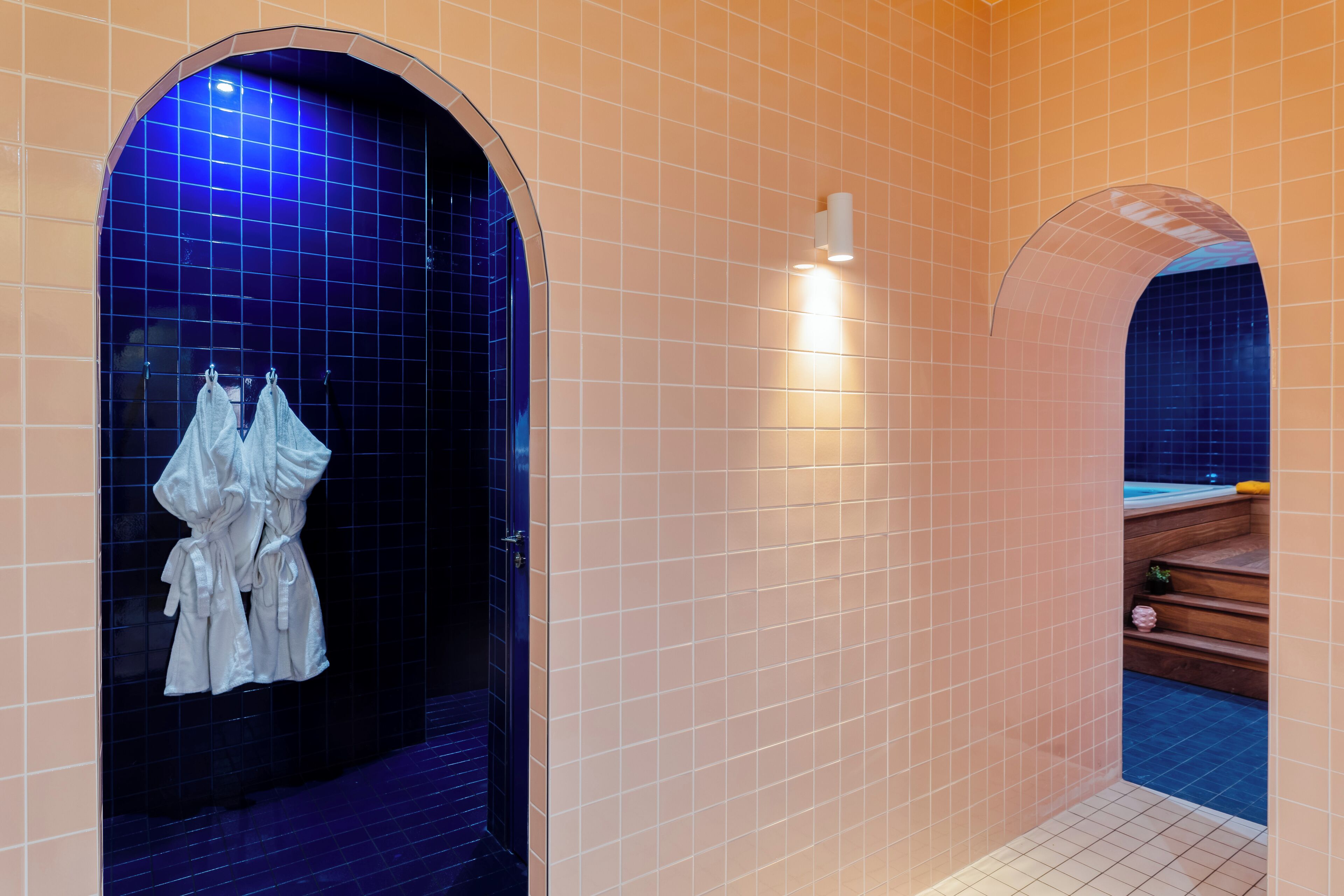 Une salle de bain avec une douche dont le carrelage est bleu, un porte-serviettes blanc et un escalier en bois menant à un jacuzzi.