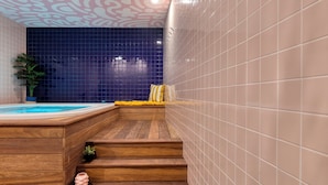 Un área de spa de madera con un jacuzzi, escalones que conducen a una pared con azulejos azules y una planta en maceta.