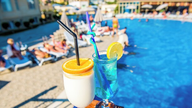 Two drinks on a tray by a poolside with lounge chairs and umbrellas in the background. - TITANIK BAKU (Baku)
