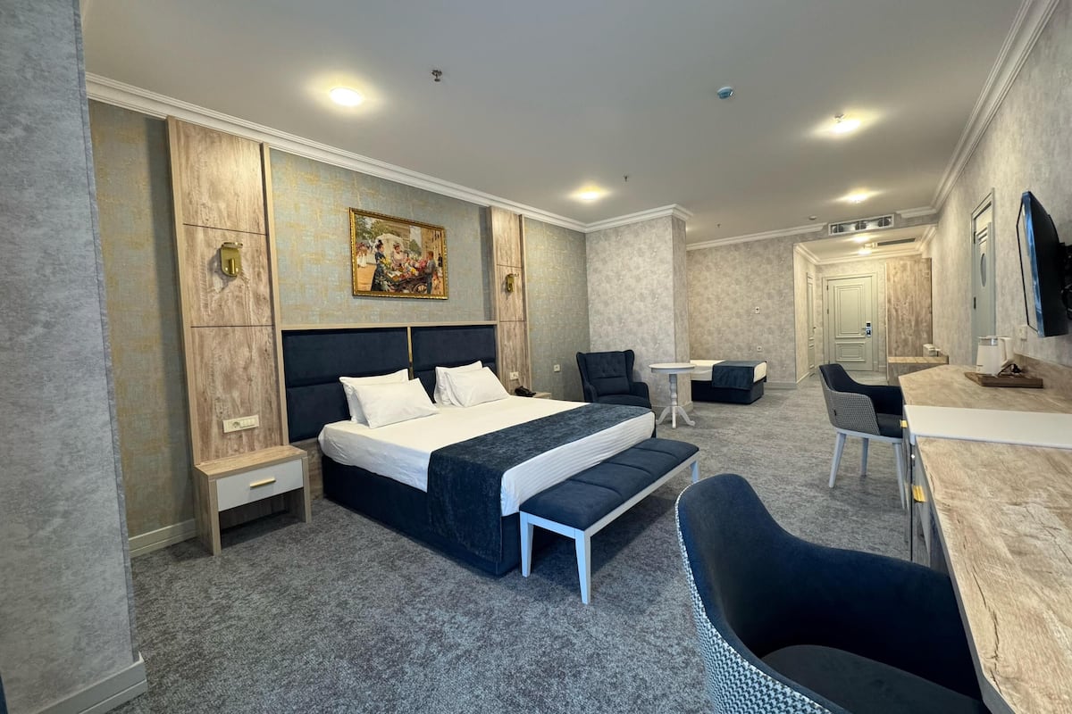 A modern hotel room with a large bed, a desk, a chair, and a small table.