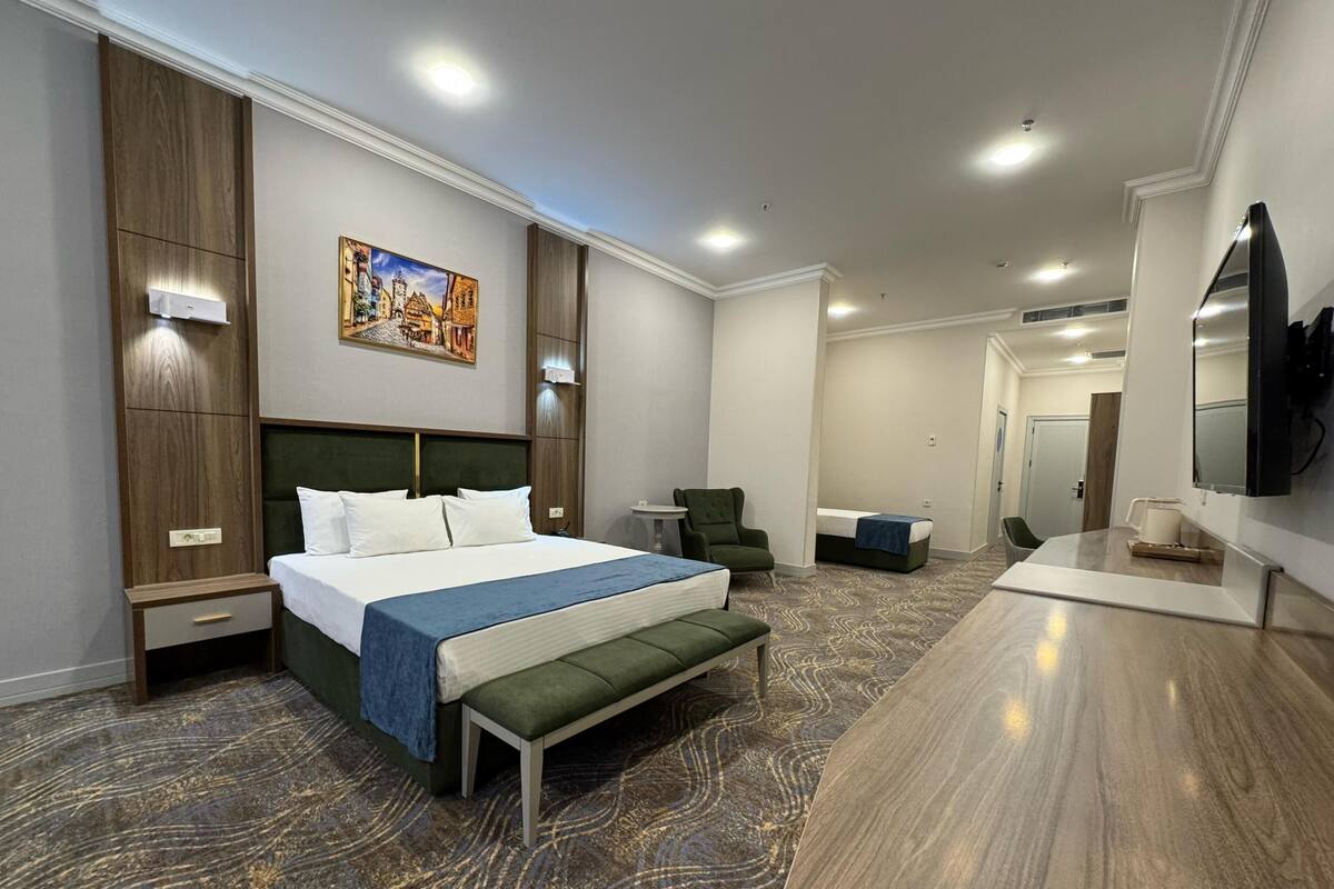 A hotel room with a large bed, a bench, a chair, a desk, and a TV.