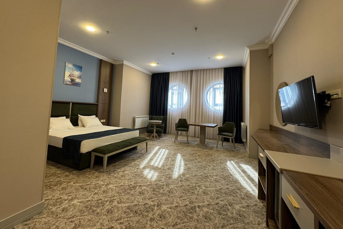 A hotel room with a bed, a desk, two chairs, a television, and a window with curtains.