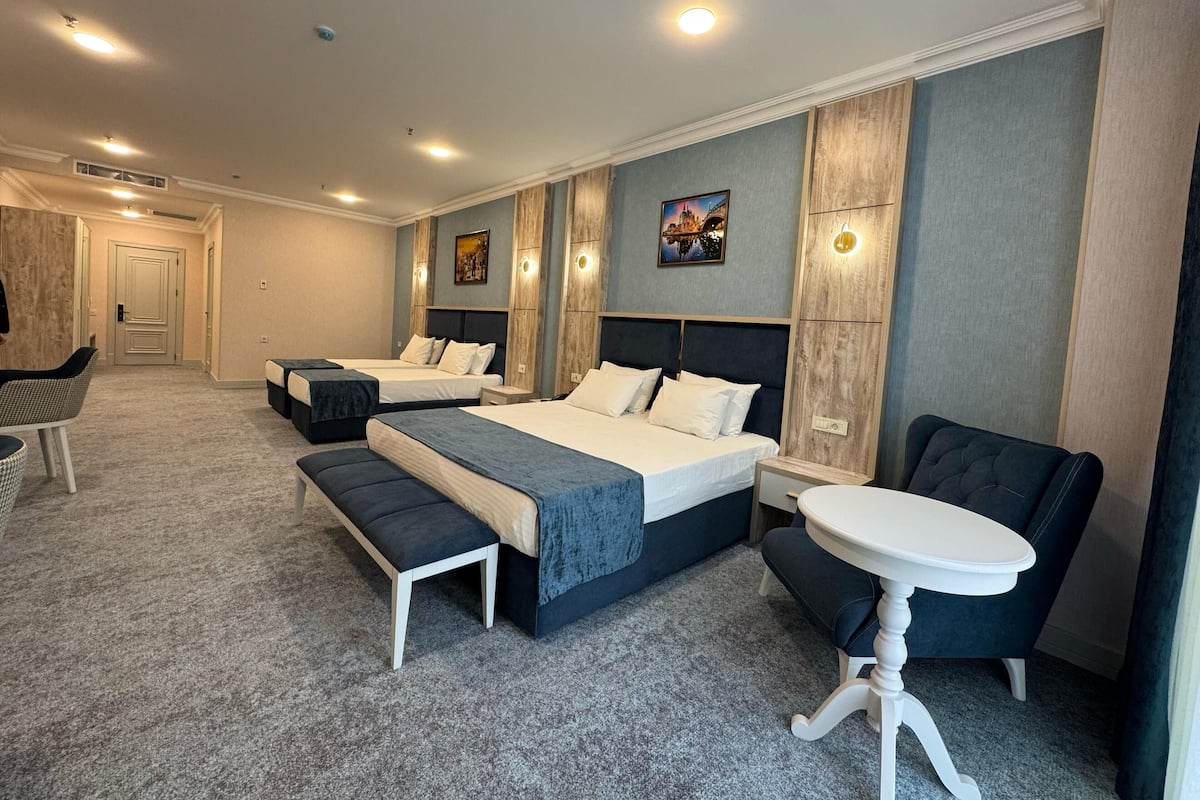 A hotel room with three beds, a bench, a round table, and a chair.